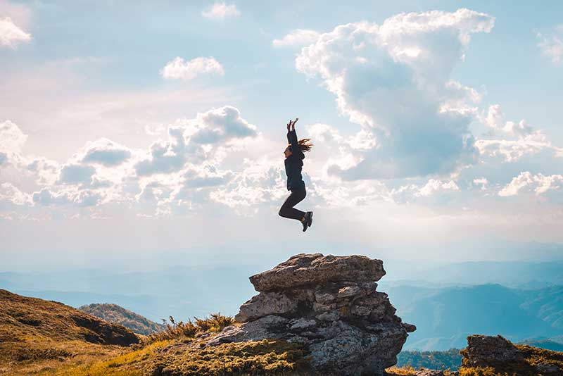 Woman jumping above a large rock